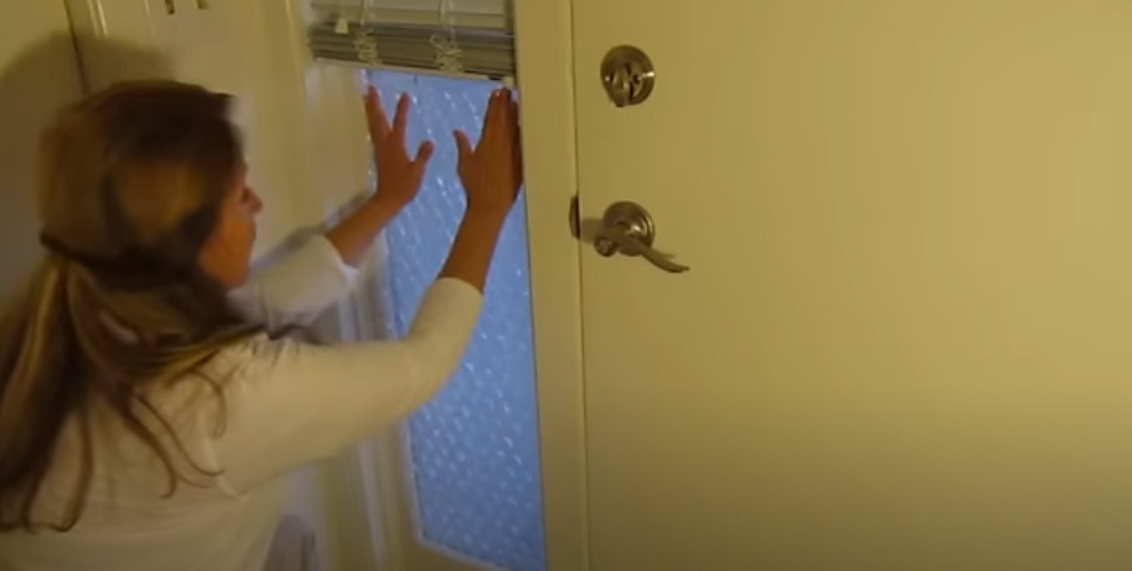 a woman covers the window by the front door with bubble wrap