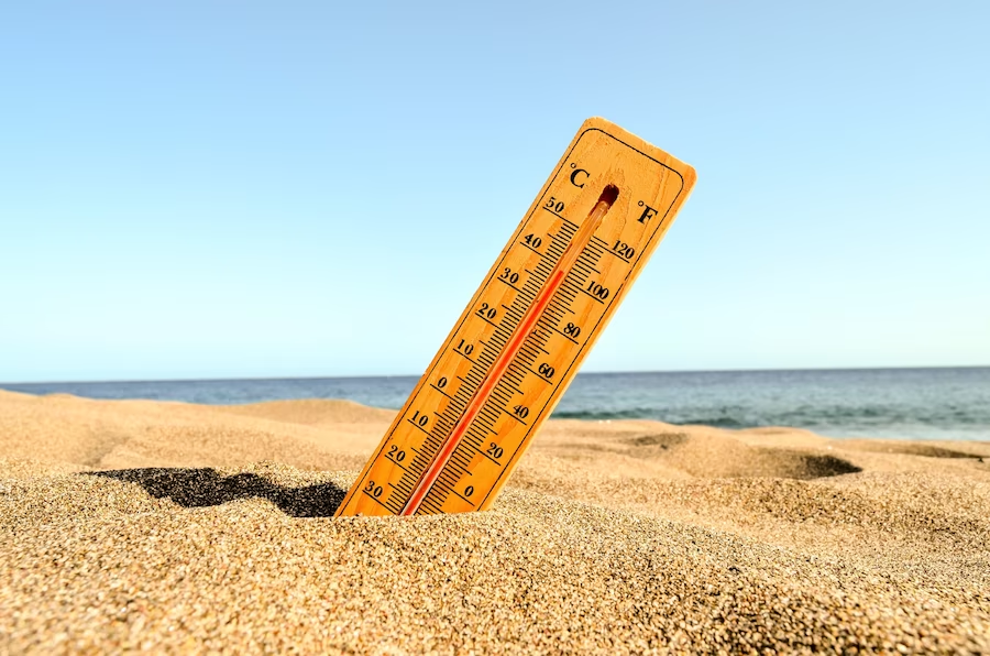 Thermometer partially buried in beach sand under the sun