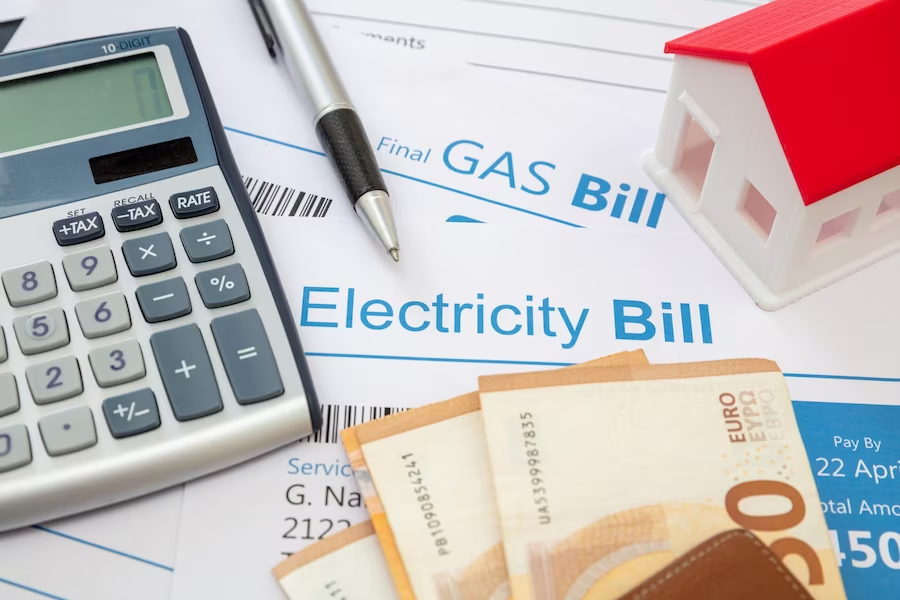 Table with calculator, pen, dollar bill, miniature house, and electrical bill