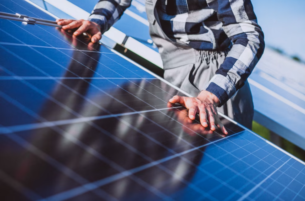 man in a shirt stands near the solar panel and touches it with his hands