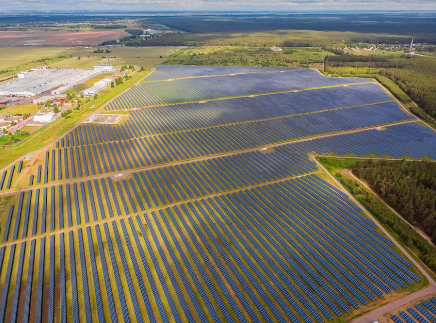 multiple solar panels in the field, building and trees - aerial view